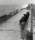 Black and white photograph showing two nuns sitting on a bench on a promenade facing the sea