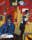 Painting by R. B. Kitaj depicting a red room with geometric shapes in an abstract suggestion of an interior. A man wearing a blue jcaket and glasses sits at a table and a woman stands next to him. A small boy and girl stand in the background