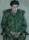 A boy wearing a green workshirt and trousers sits ina chair with his hands clasped in his lap.