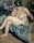 A female nude sitting in a dingy bedroom with her legs crossed and resting her chin on her hand facing away from the viewer.