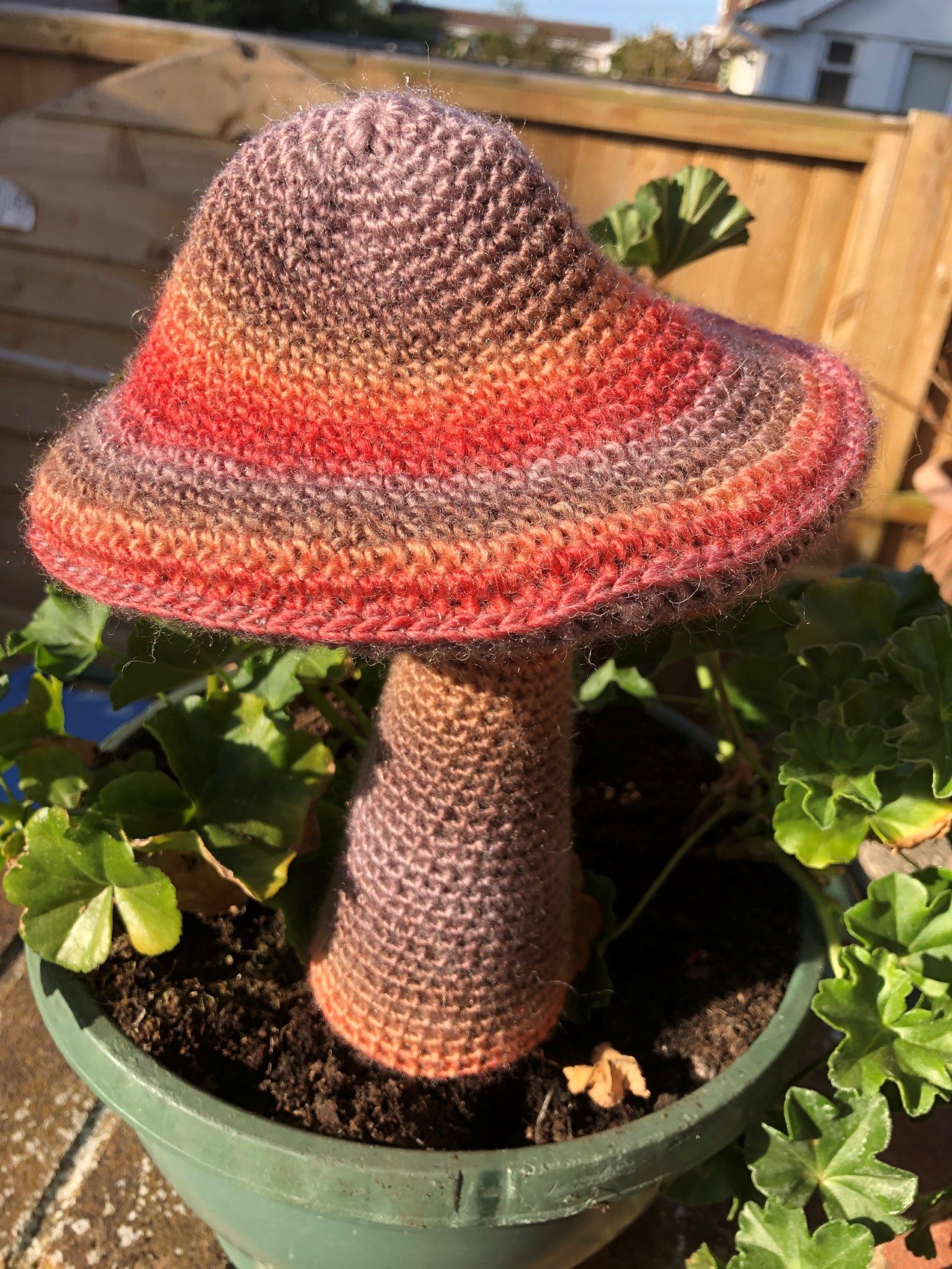 A larger than life multi-coloured crocheted mushroom sits in a plant pot.