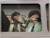 Photograph of two men with their hands cuffed together, shielding their faces from the viewer. The photograph is encased in a metal frame made to look like the door of a car.