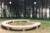 Round stone bench on grass with trees in the background