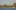 Photograph of a harbour with water at bottom with 4 sailing yachts and in the background a line of trees with the spire of Chichester Cathedral in the middle
