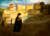 Painting of a woman in long black dress with a young child walking along the shore with Tenby in the background