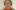 Headshot of a lady with shoulder length brown grey hair and a grey jumper with orange collar