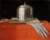 Painting of a rounded silver casket sat on tap of a flat book, sat on top of a pair of white gloves all sat on top of a red case with a gold latch. Background is black.