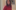 Photograph of a woman wearing a ink jumper and blue jeans with long curly brown hair stood in front of an artwork hung on a white wall. It shows an abstract head made up of many different coloured shapes.